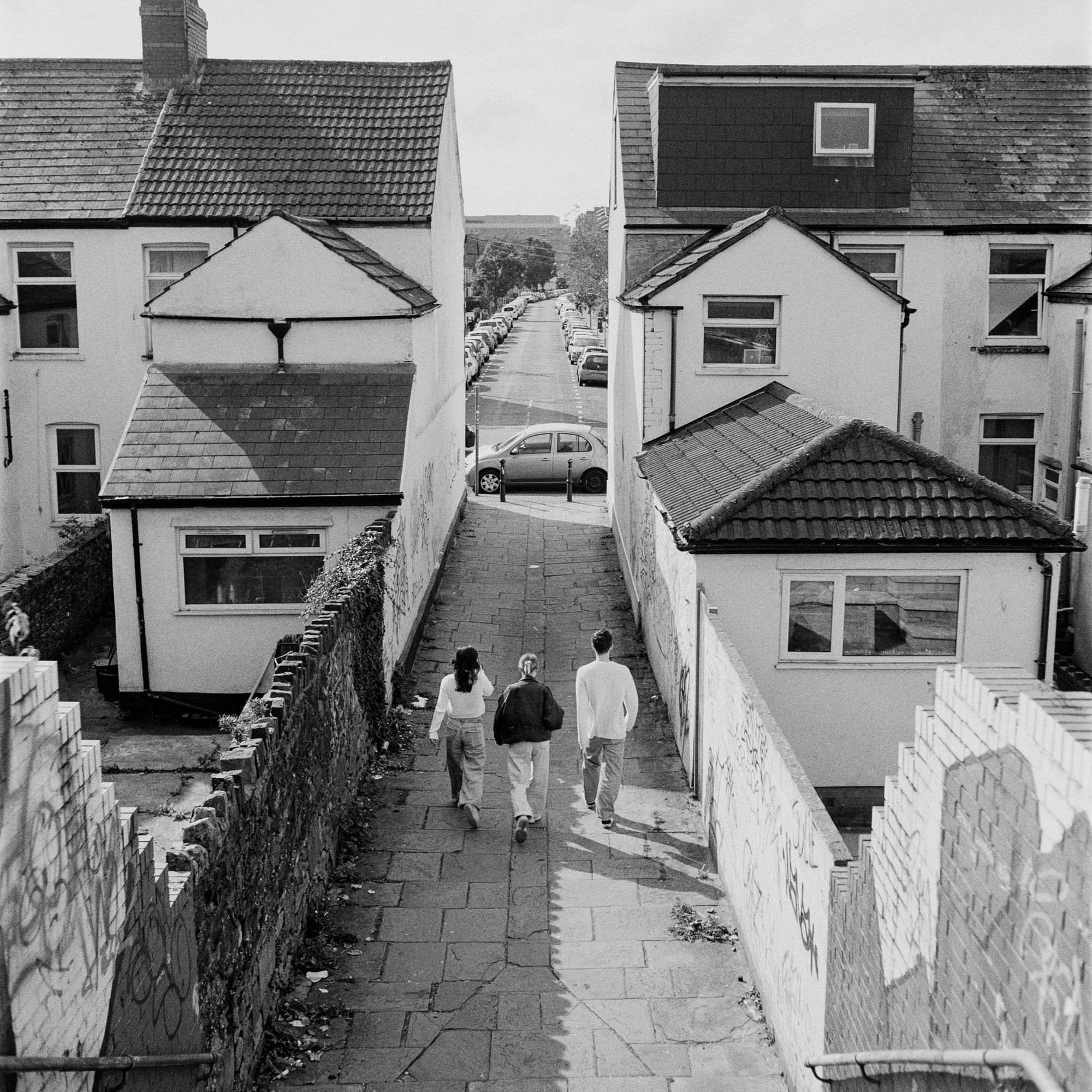 Three people walking through a narrow terraced alley in Cardiff